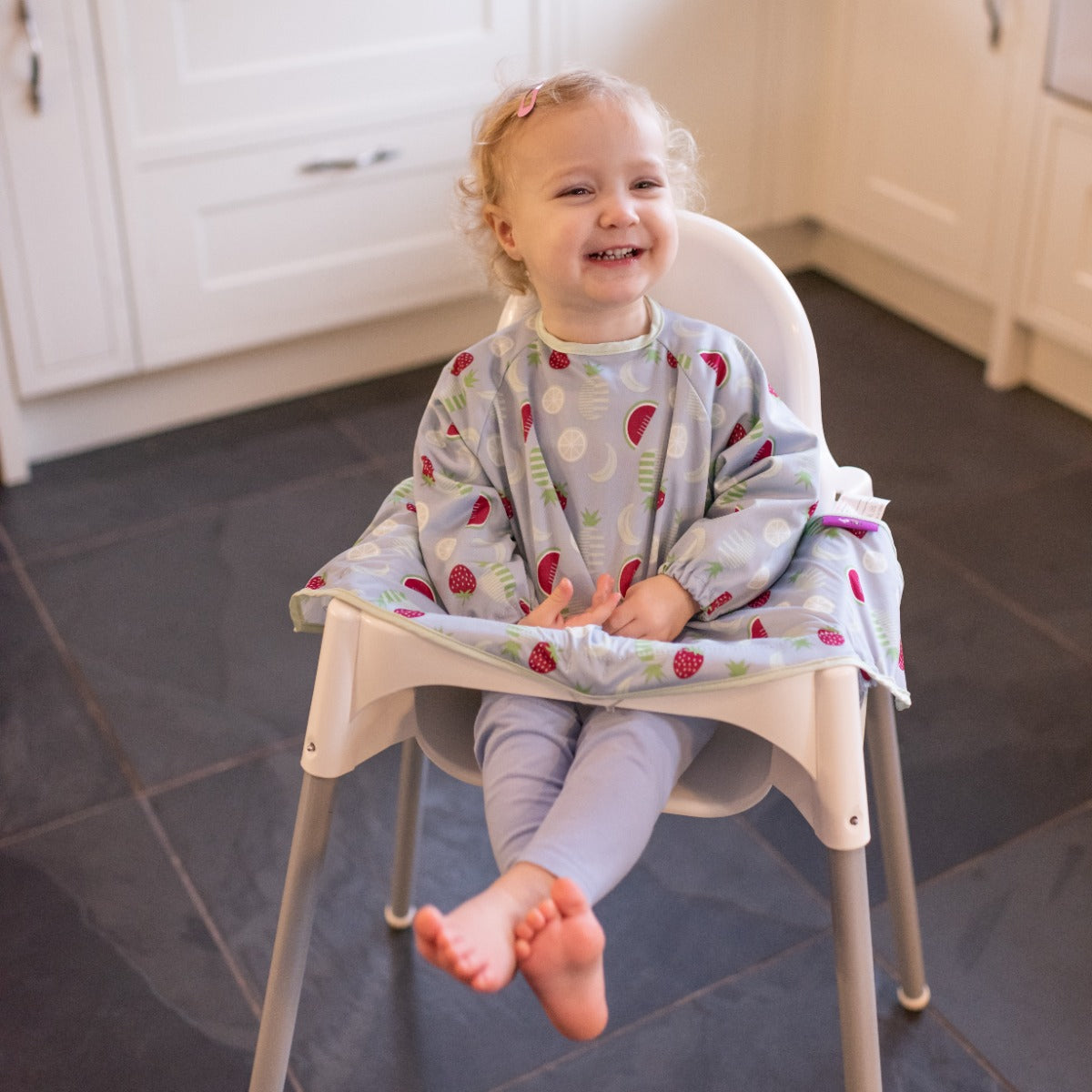 Baby girl sitting on a highchair wearing long sleeve bib with fruits print