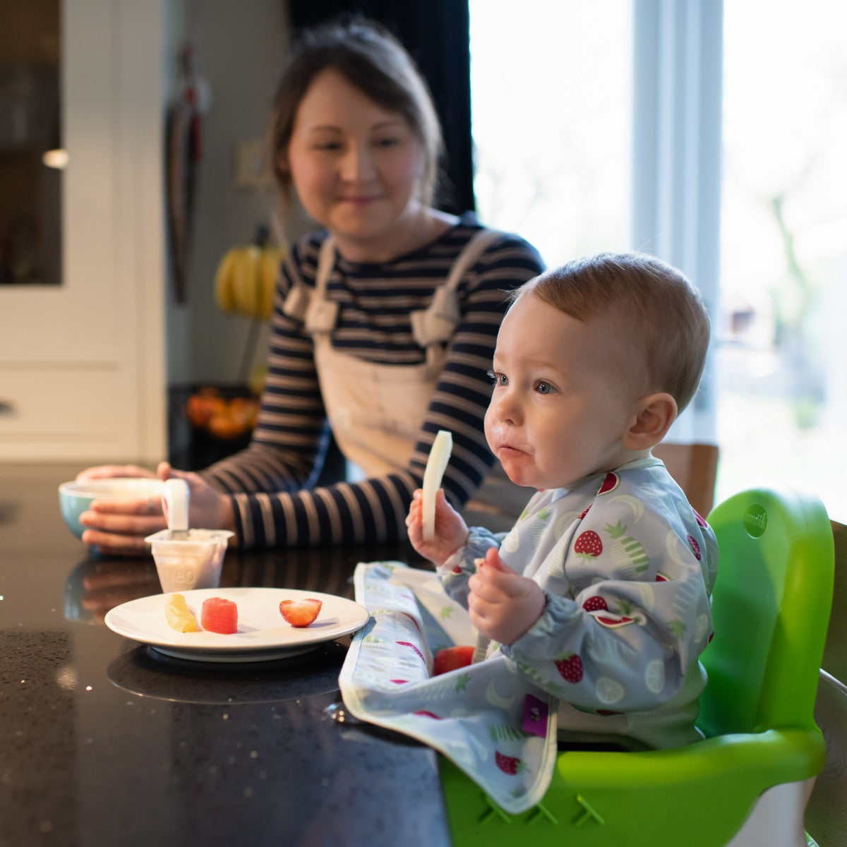 Baby eating wearing long sleeve bib with fruits print sitting on a highchair