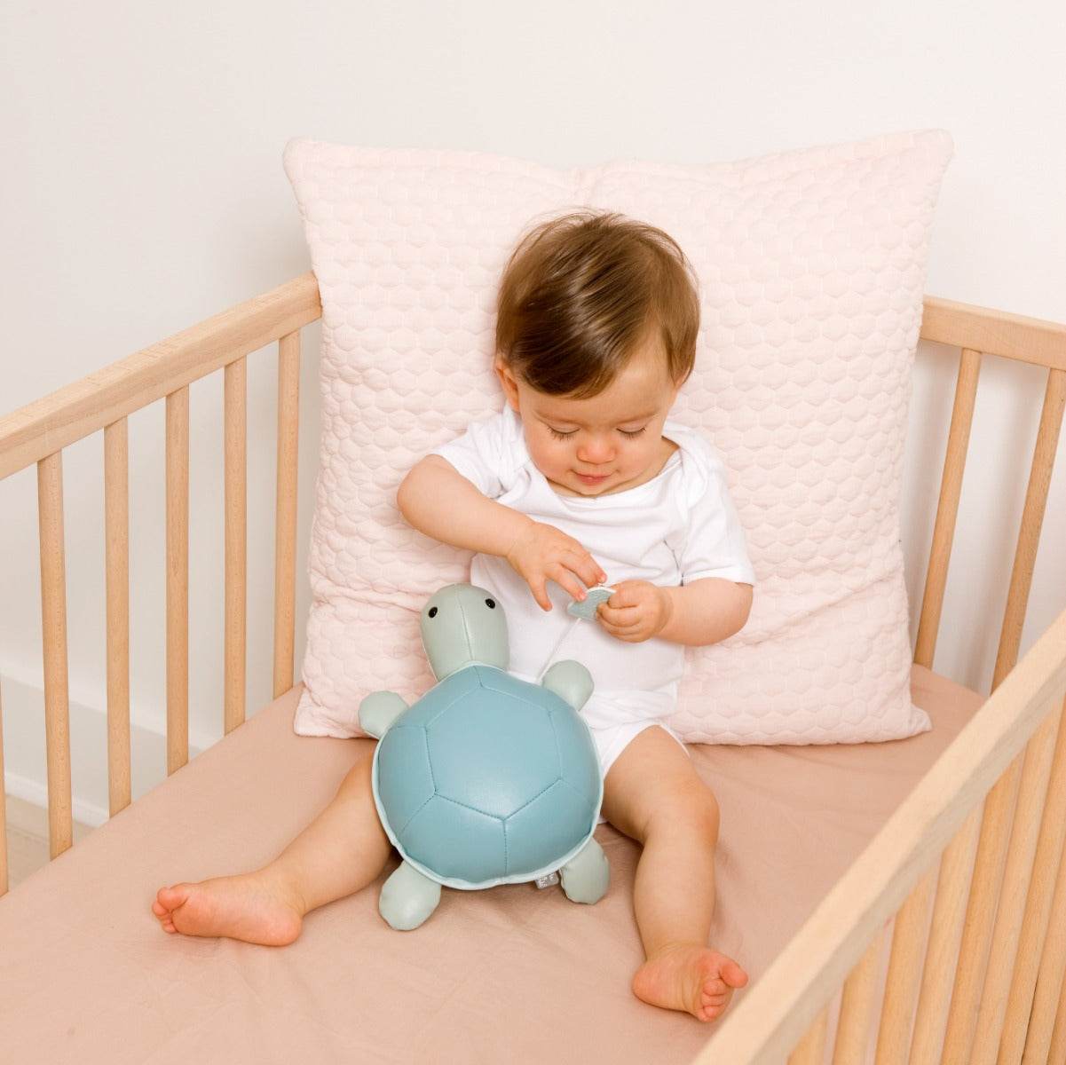 Baby holding Musical Friends - Emilie the Turtle from Little Big Friends sitting in a cot