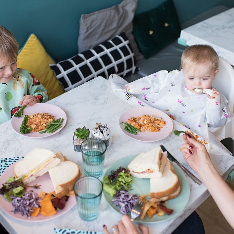Boy wearing disposable bib directly attached to a table, sitting on highchair eating food.