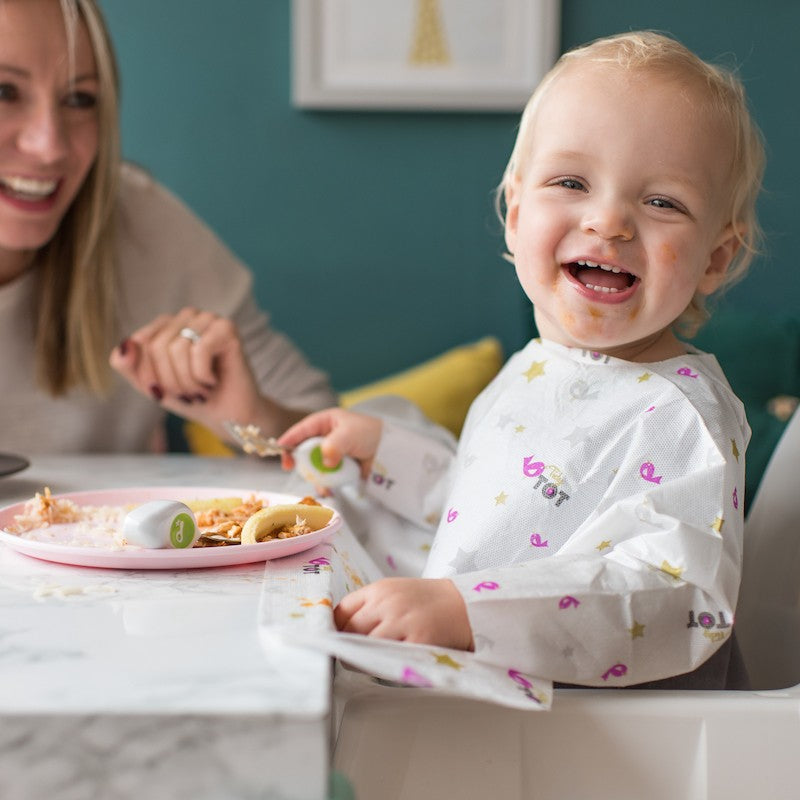 Baby boy eating food having disposable bib on and mother is worry free