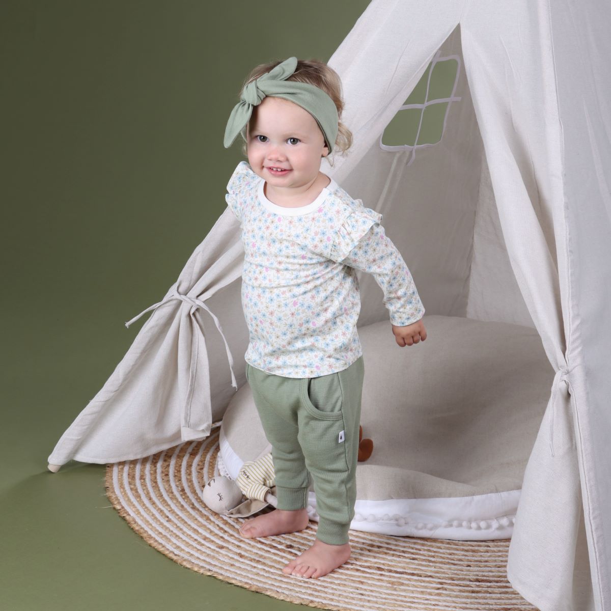 Baby girl wearing Arctic Adventure Merino Pants in Moss in Moss colour from dimples New Zealand pairing it with head band and frill top