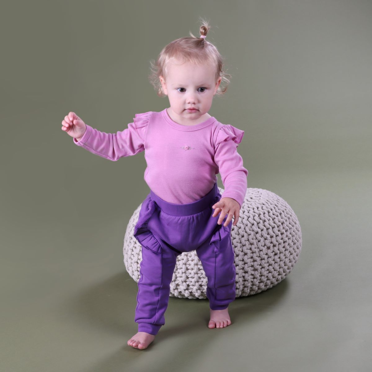 Baby wearing Orchid Merino frill bodysuit pairing it with purple pant