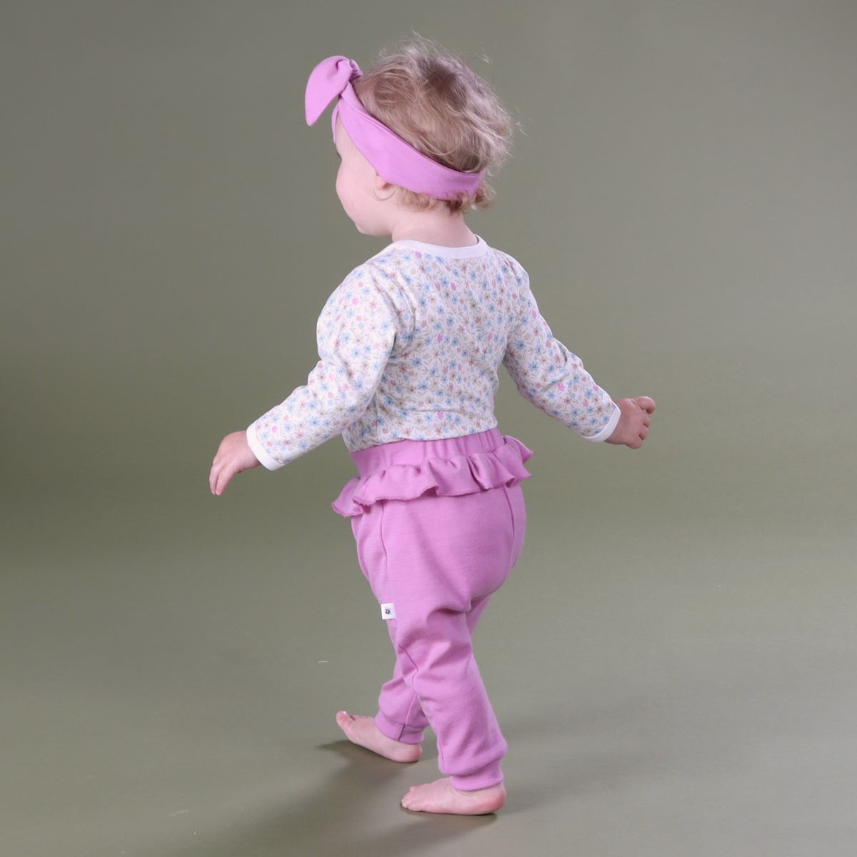 Baby girl wearing merino frill pants and head band pairing it with floral bodysuit rear view