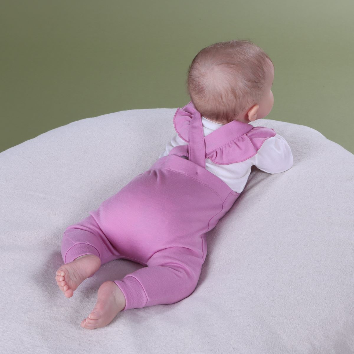 Baby wearing orchid merino frill overall and pairing it with merino long sleeve bodysuit sitting on a pillow