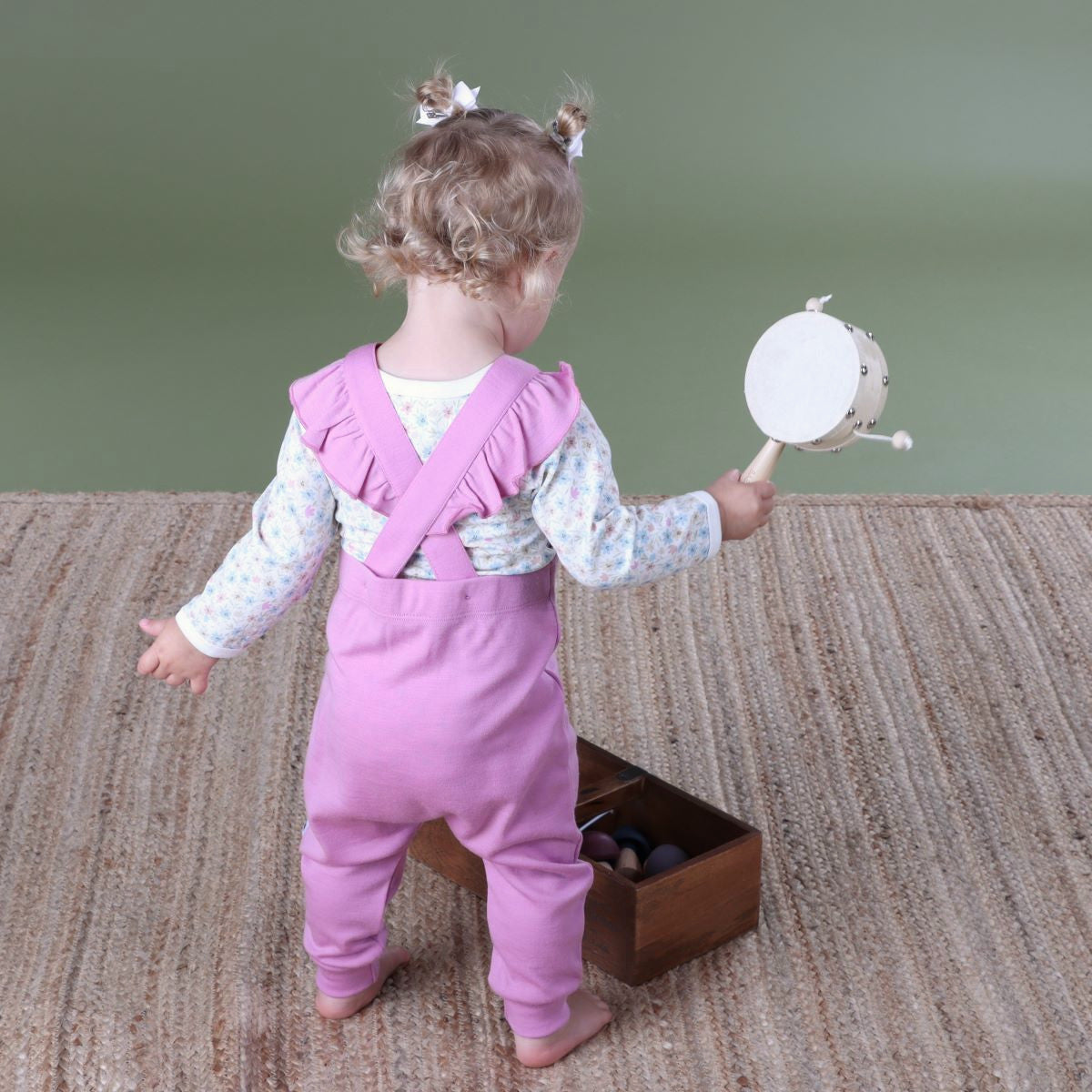 Baby wearing orchid merino frill overall and pairing it with wildflower long sleeve bodysuit playing in a room