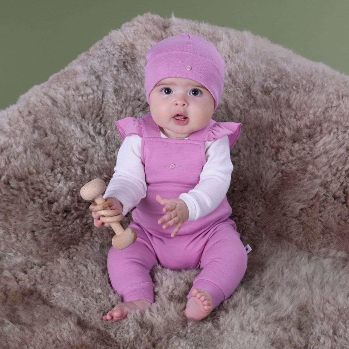 Baby wearing orchid merino frill overall and pairing it with merino long sleeve bodysuit sitting on a rug