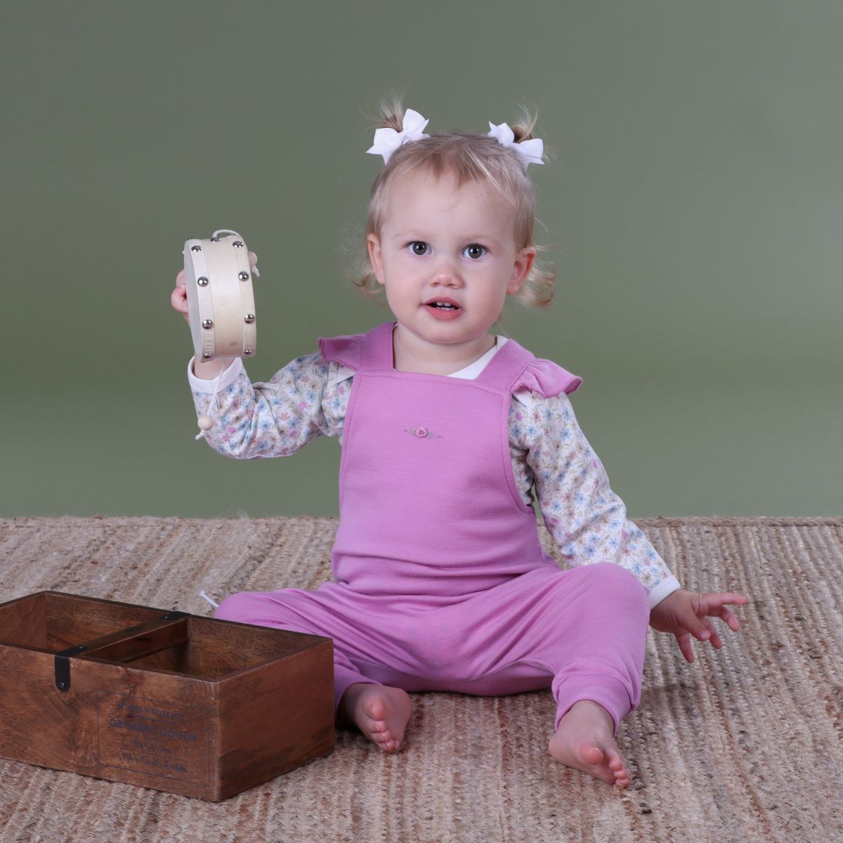 Baby wearing orchid merino frill overall and pairing it with wildflower long sleeve bodysuit  playing in a room