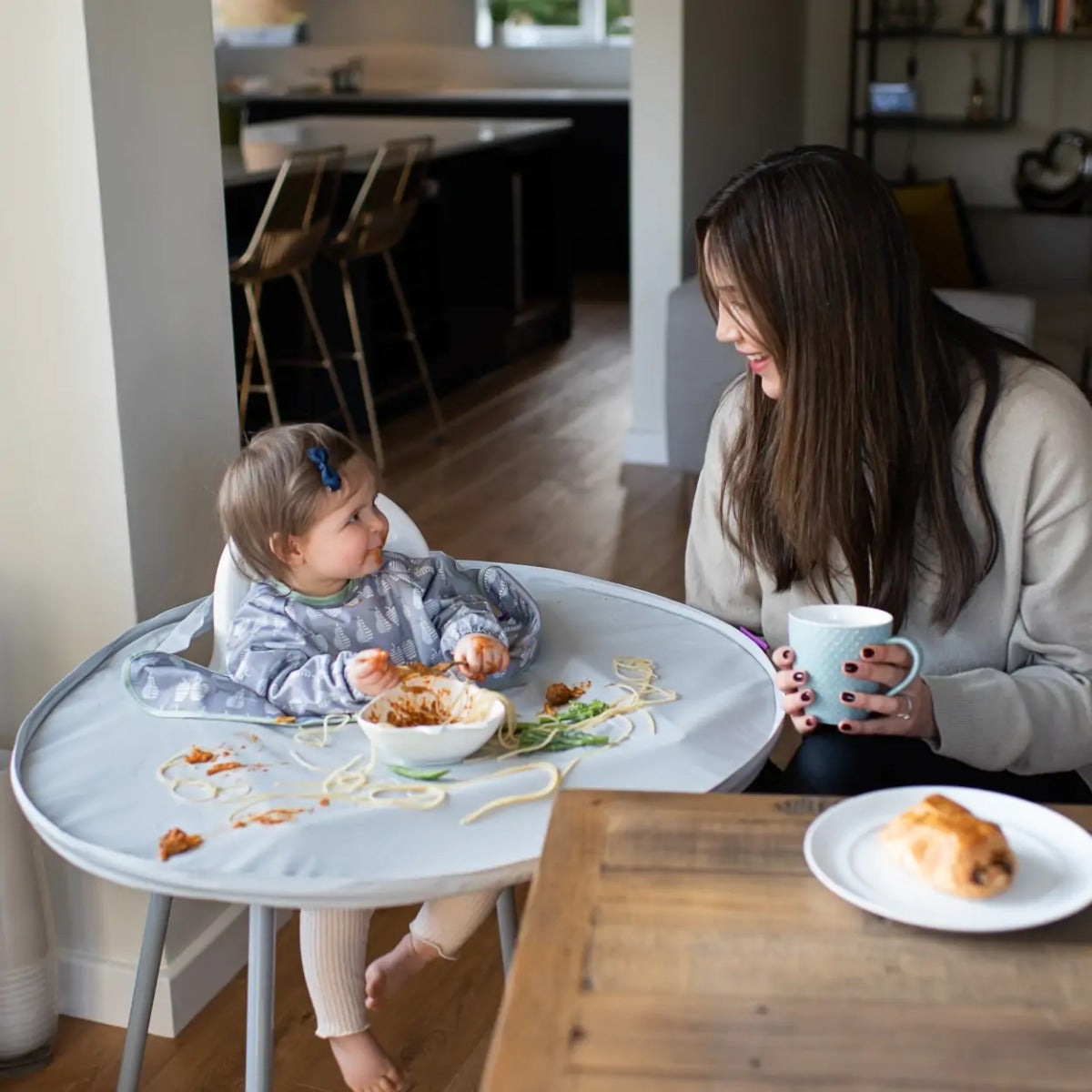 Baby eating with Tidy Tot tray around highchair and long sleeve bib, happy mother sitting beside baby