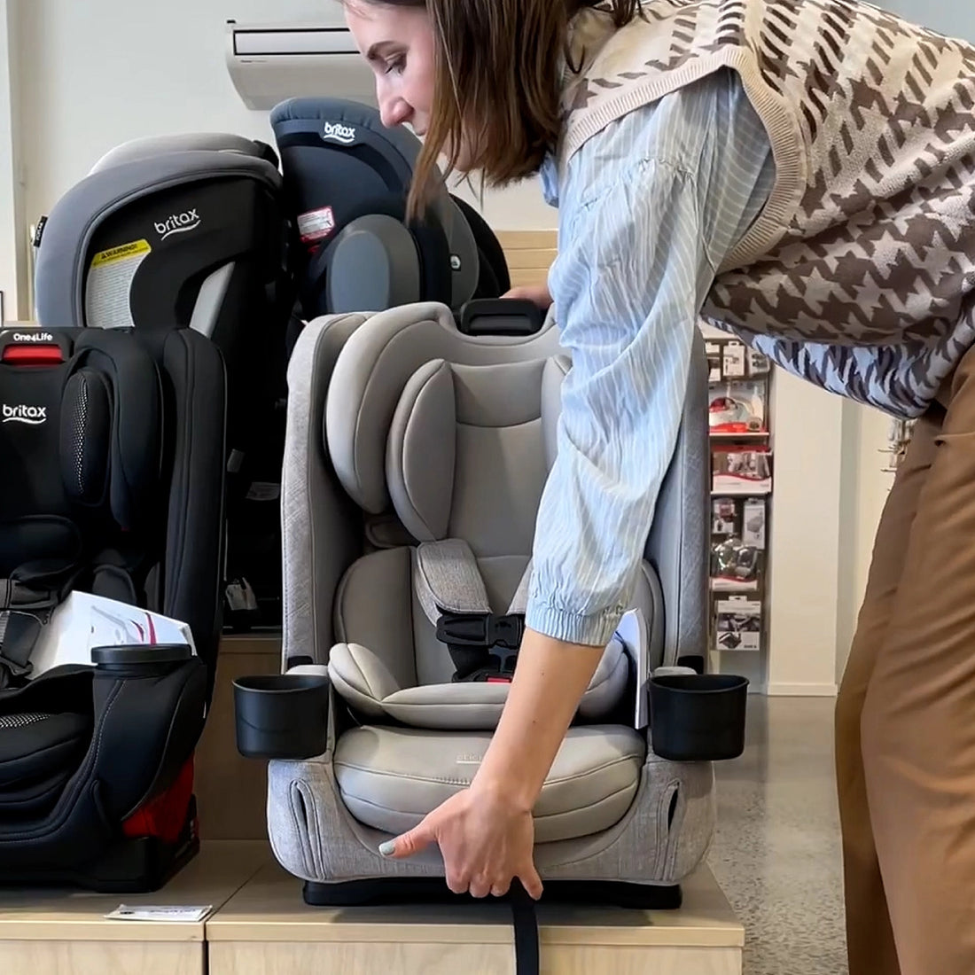 Woman inspecting a car seat in a store with multiple car seats displayed.