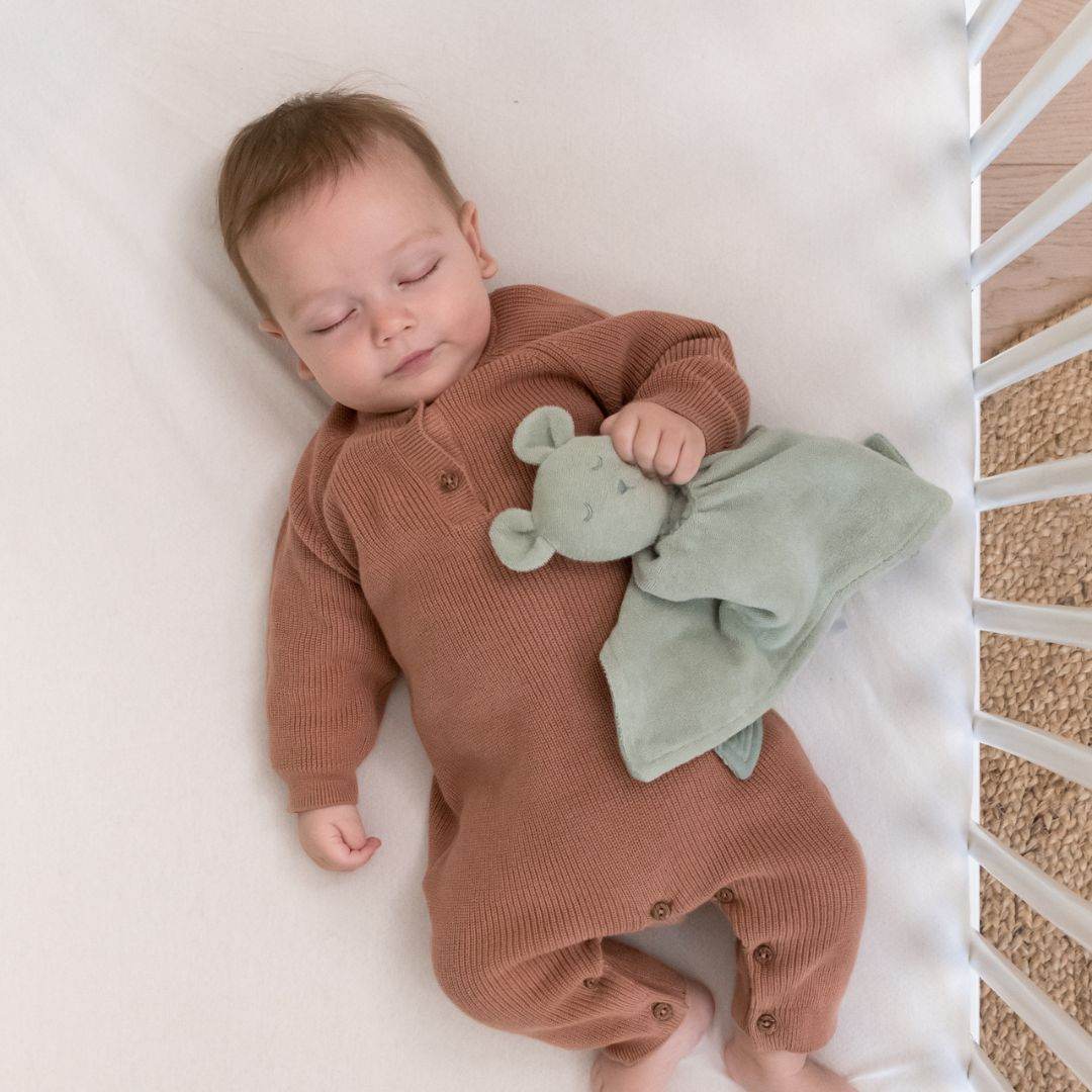 Baby sleeping peacefully in cot holding doomoo bunny detachable baby soother in sage green