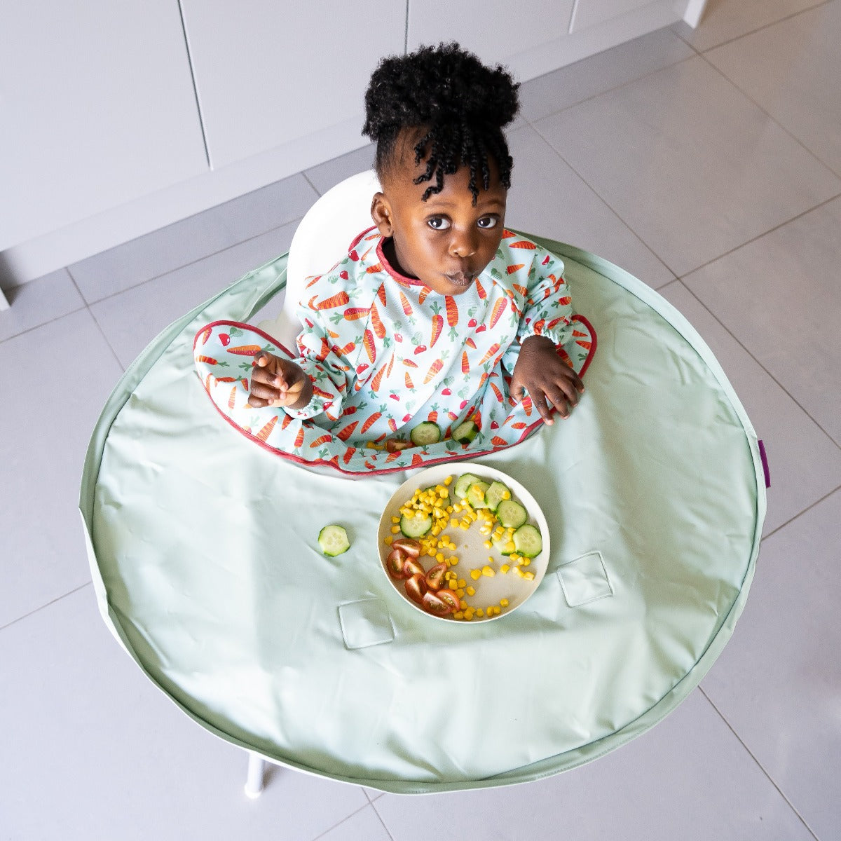 Baby eating with Tidy Tot tray around highchair and long sleeve carrots bib
