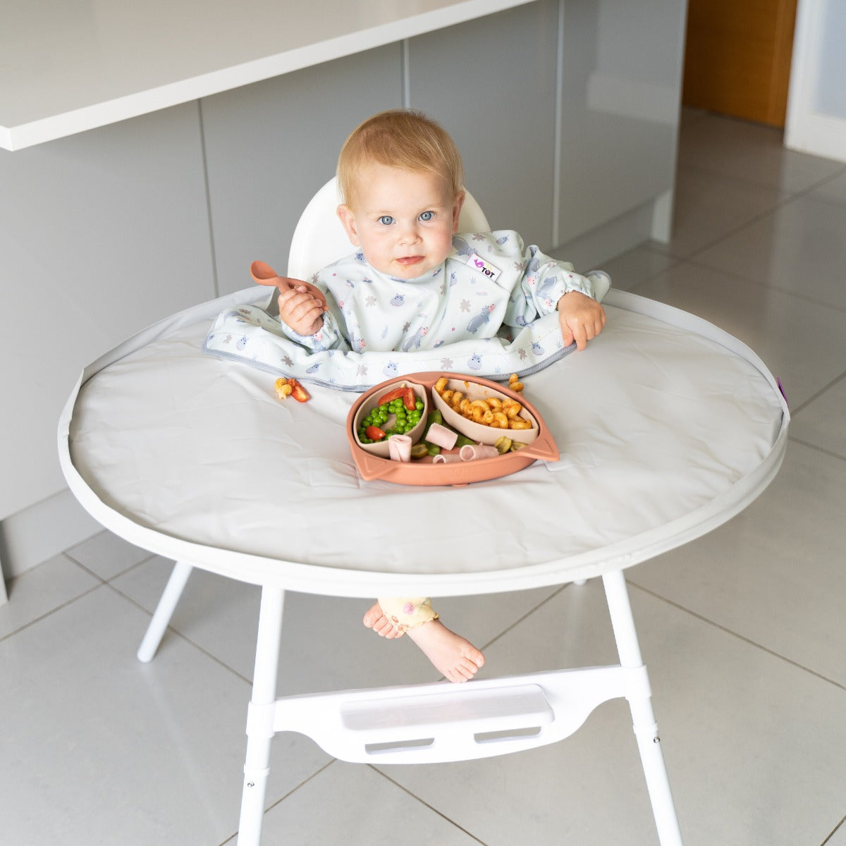 Baby sitting on a highchair wearing coverall long sleeve bib with hippo print for no mess