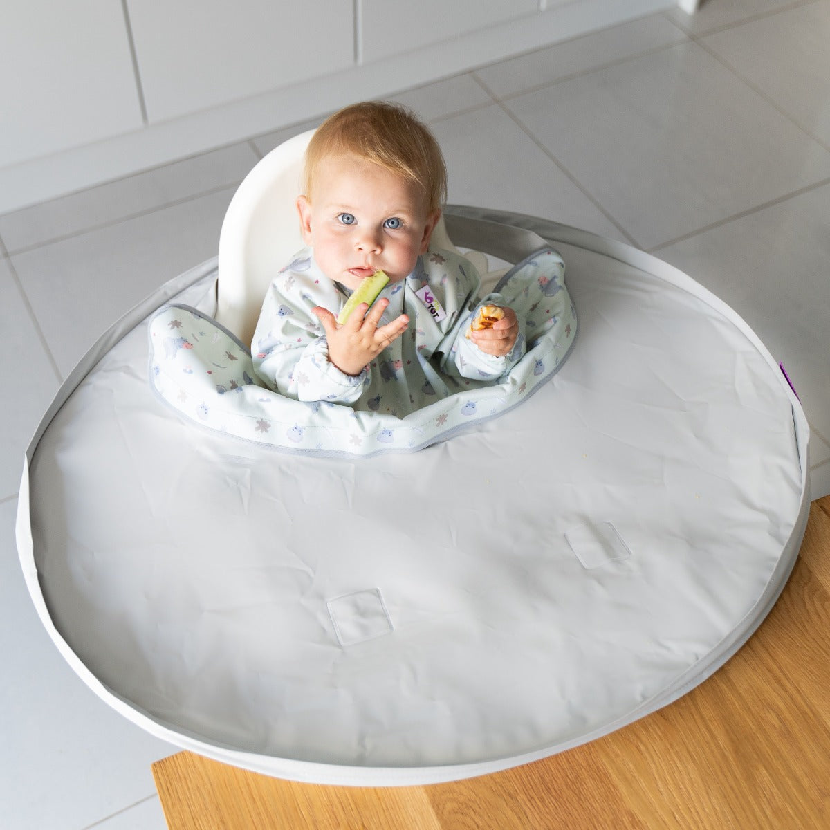 Baby eating on a highchair wearing overall long sleeve bib with hippo print