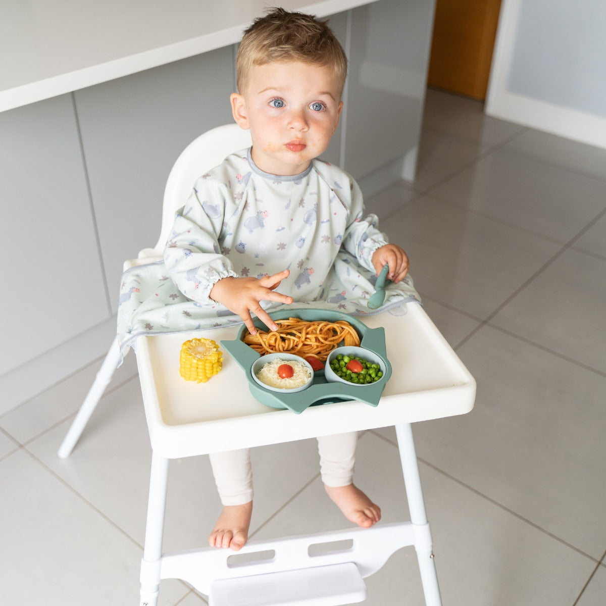 Baby eating on a highchair wearing long sleeve bib with hippo print