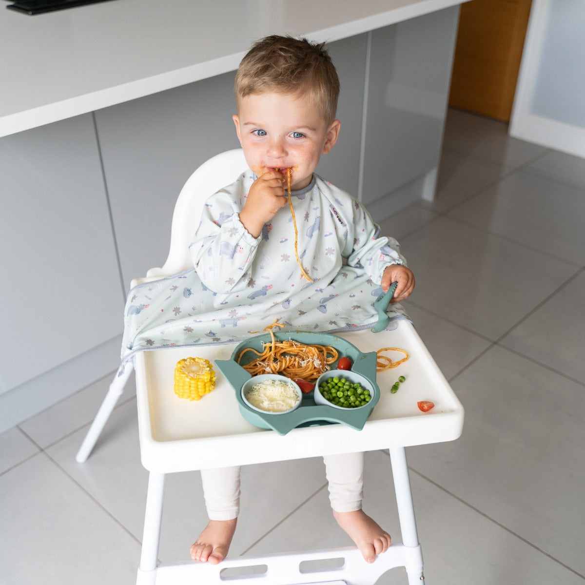 Baby eating on a highchair wearing long sleeve bib with hippo print