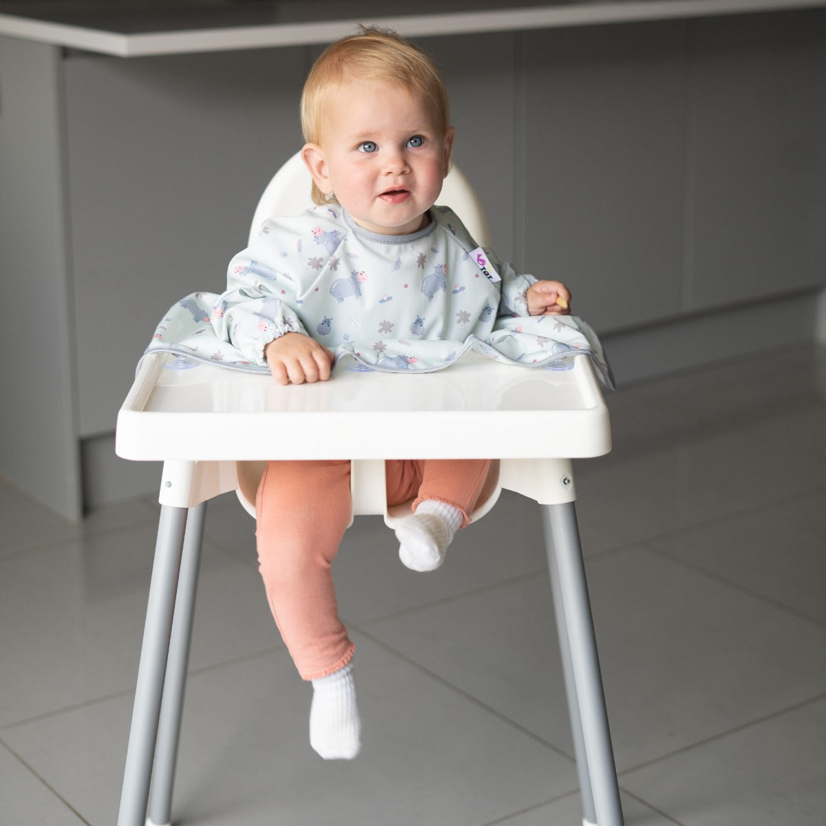 Baby on a highchair wearing long sleeve bib with hippo print