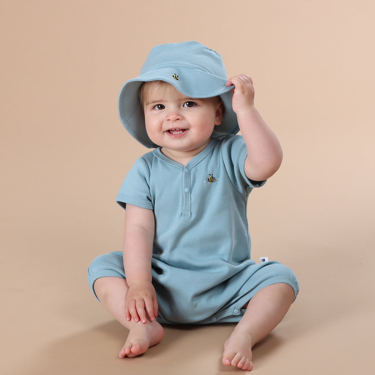 Baby girl wearing Ocean Cotton romper and sunhat while smiling