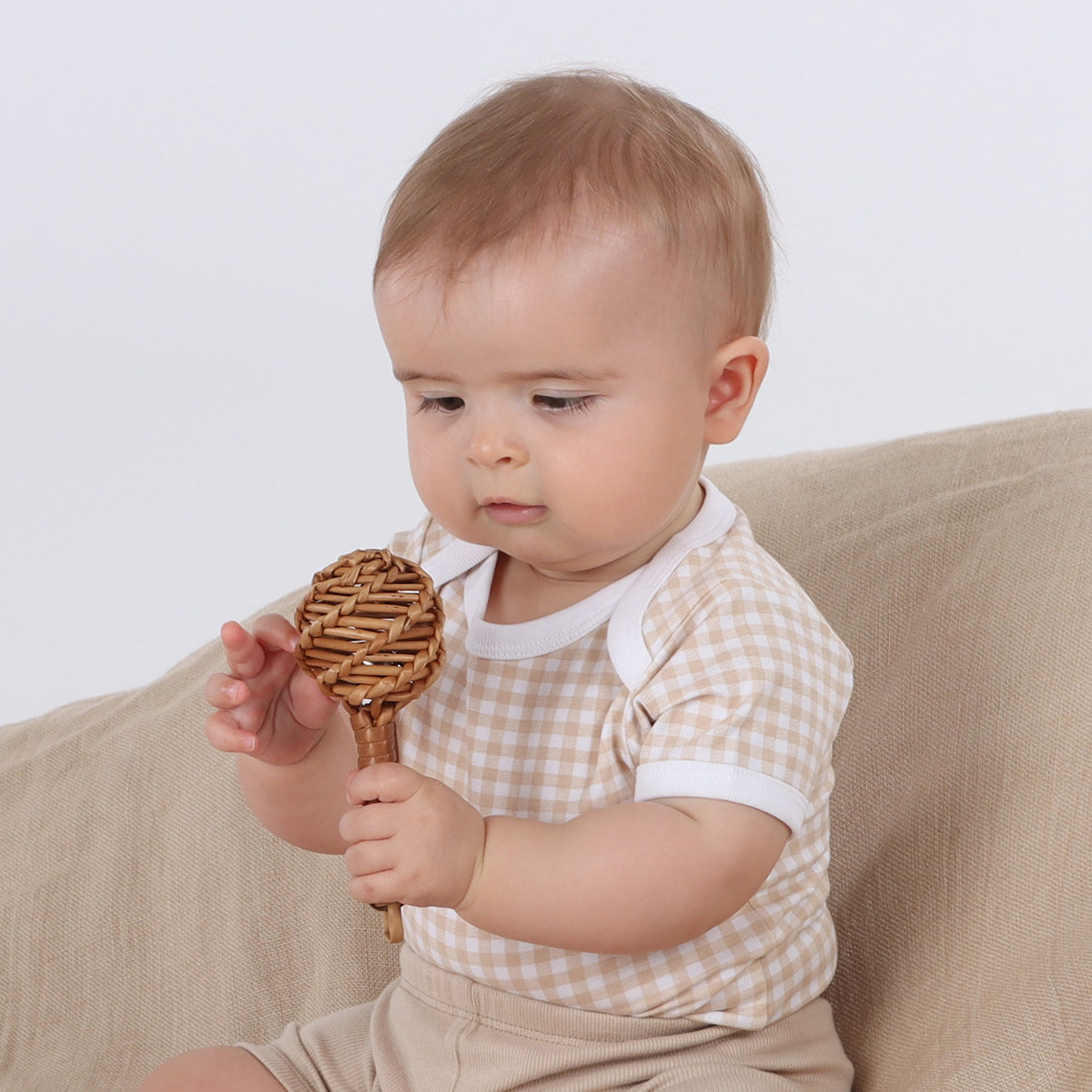 Baby wearing Organic cotton gingham bodysuit and playing with rattle