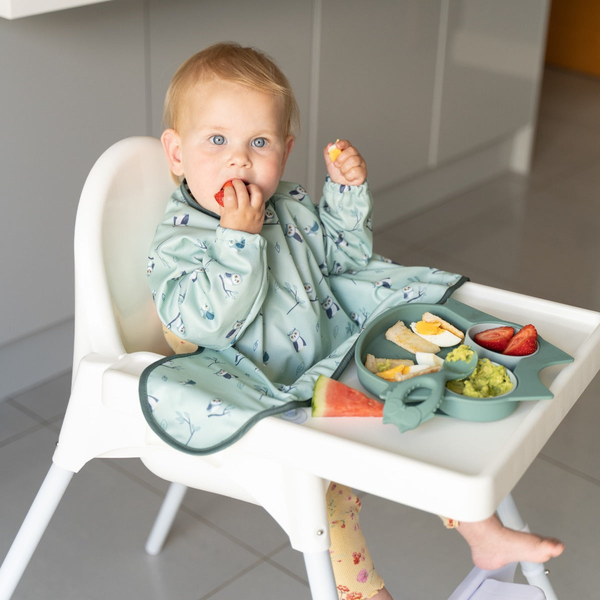 Baby eating on a highchair wearing long sleeve bib with owl print