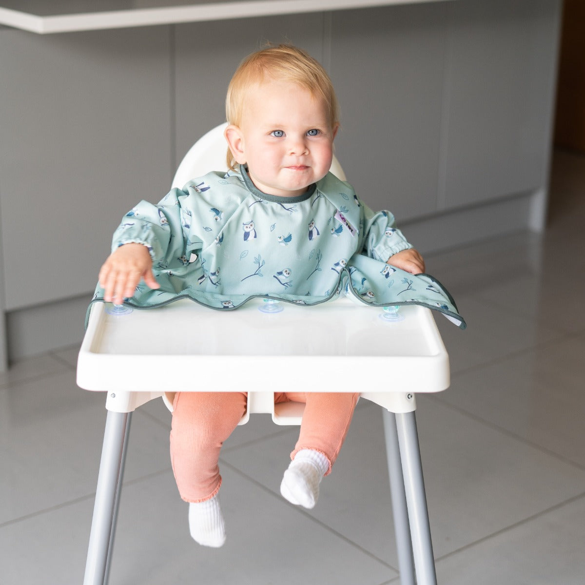 Baby eating on a highchair wearing long sleeve bib with owl print