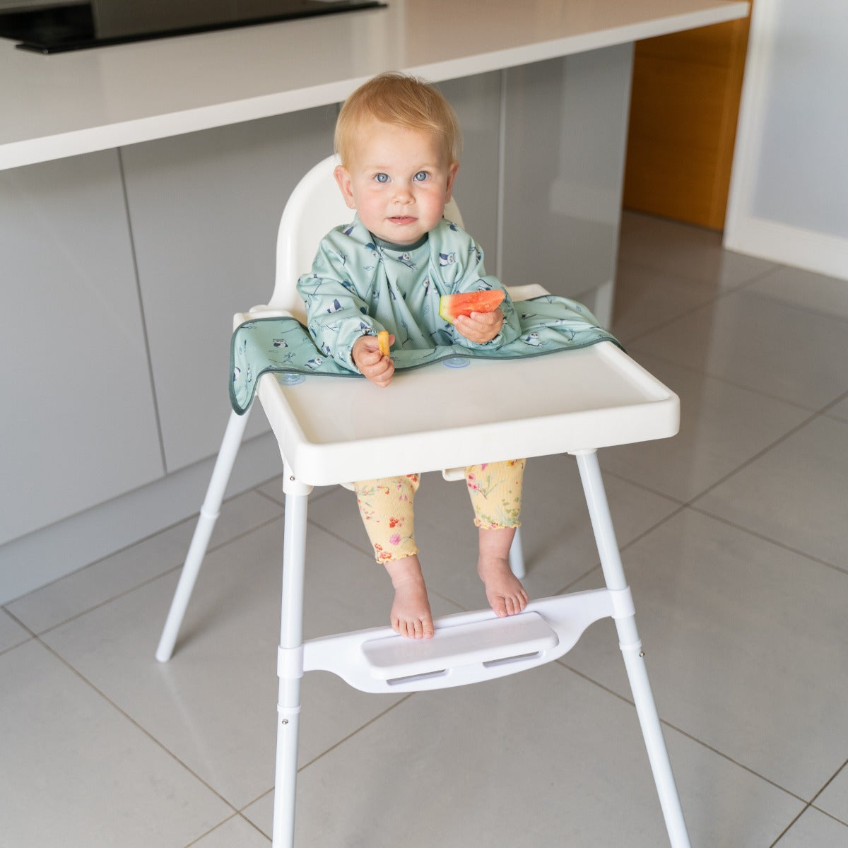Baby eating on a highchair wearing long sleeve bib with owl print