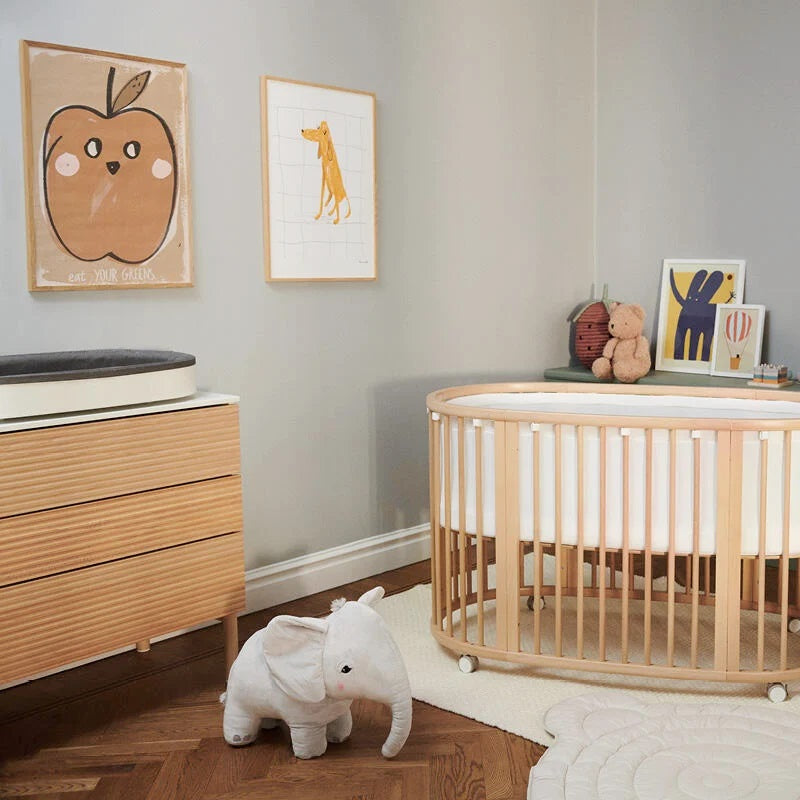 Nursery room with wooden crib, dresser, and toys on a light gray wall.