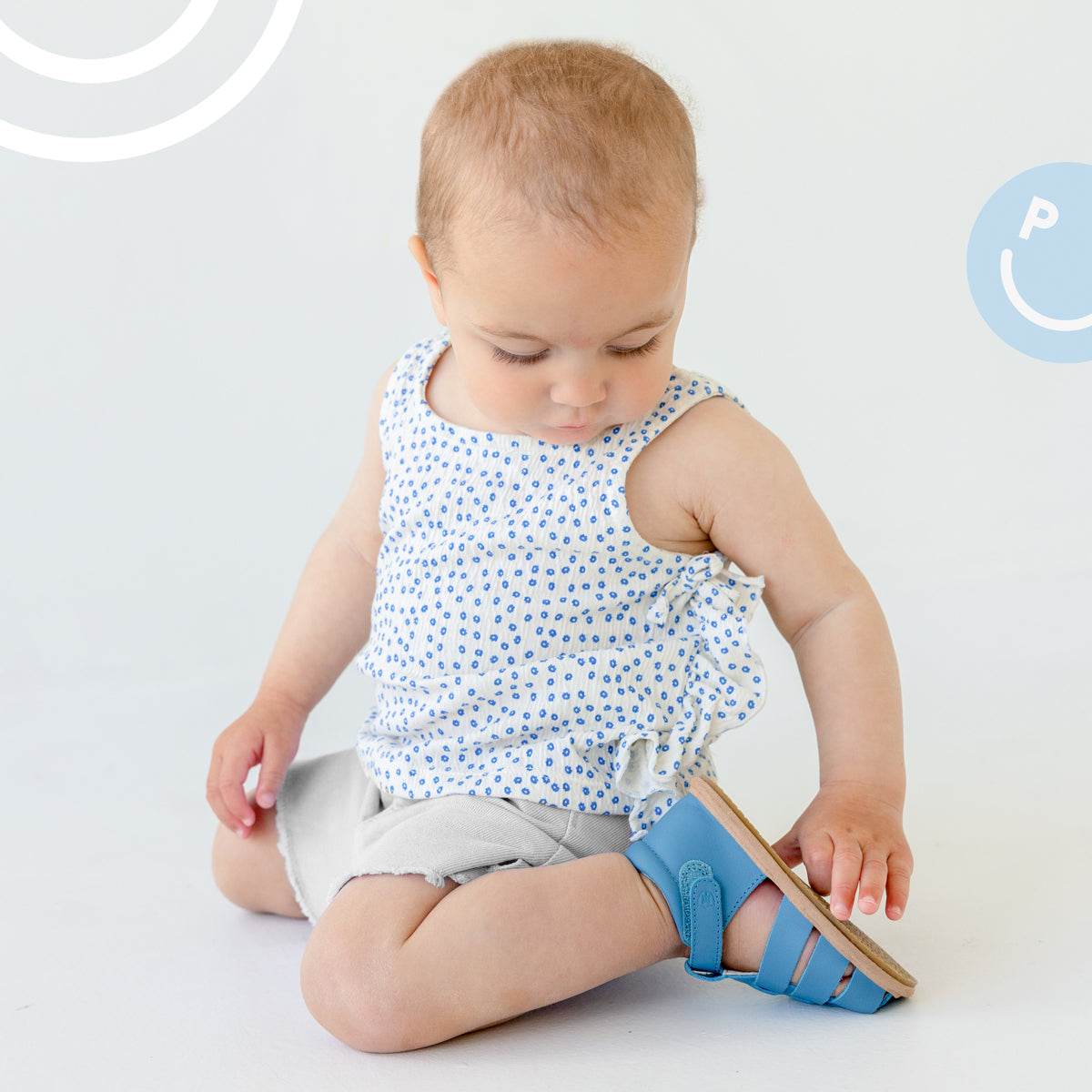 Baby sitting down wearing Pretty Brave Rio Baby Sandals in Playground Blue side