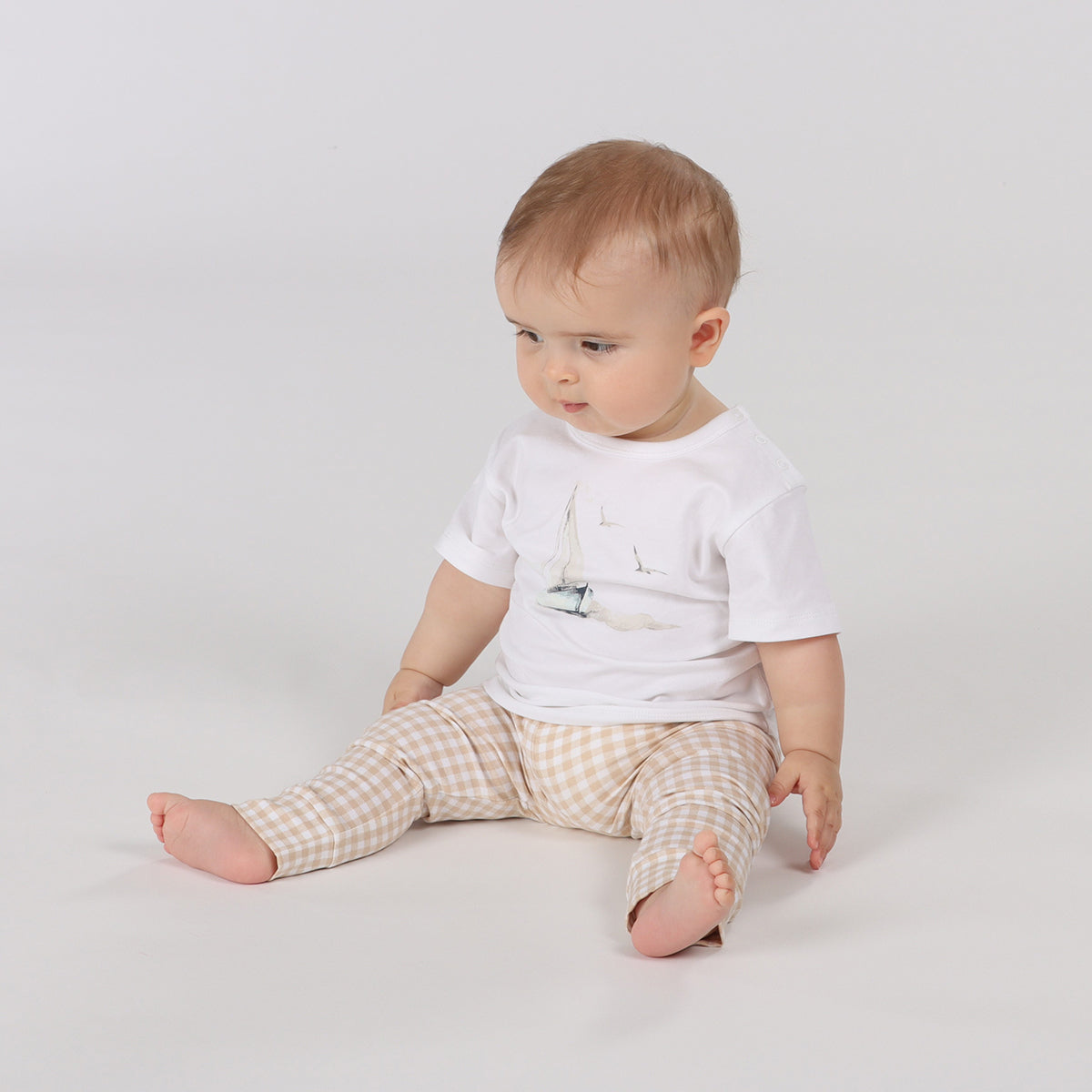 Baby sitting wearing Organic cotton T-shirt  with sailing boat graphic and ghingham leggings