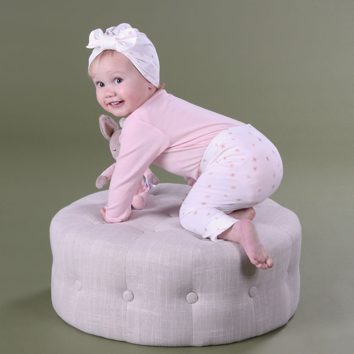 Baby girl wearing dainty floral cotton legging with merino long sleeve top and cotton beanie playing on an ottoman