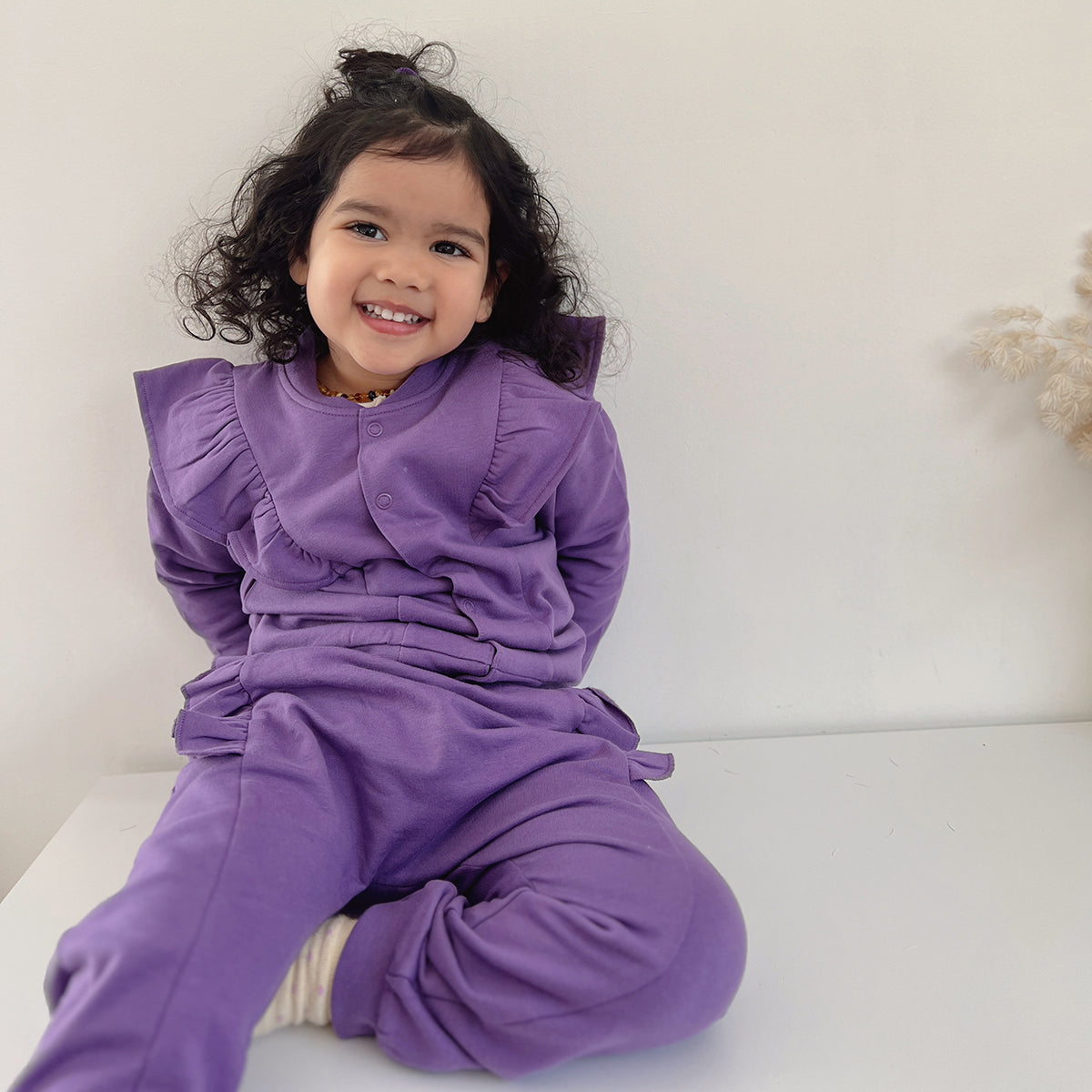 Baby girl sitting with a basket wearing Cotton Fleece Frill Jacket pairing it with pant and merino top