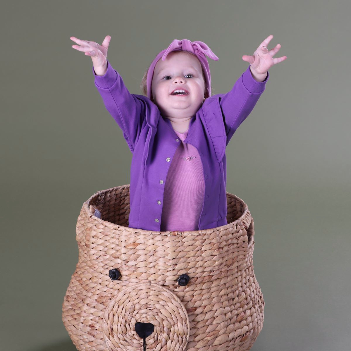 Baby girl standing inside a basket wearing Cotton Fleece Frill Jacket pairing it with pant, headband and merino top