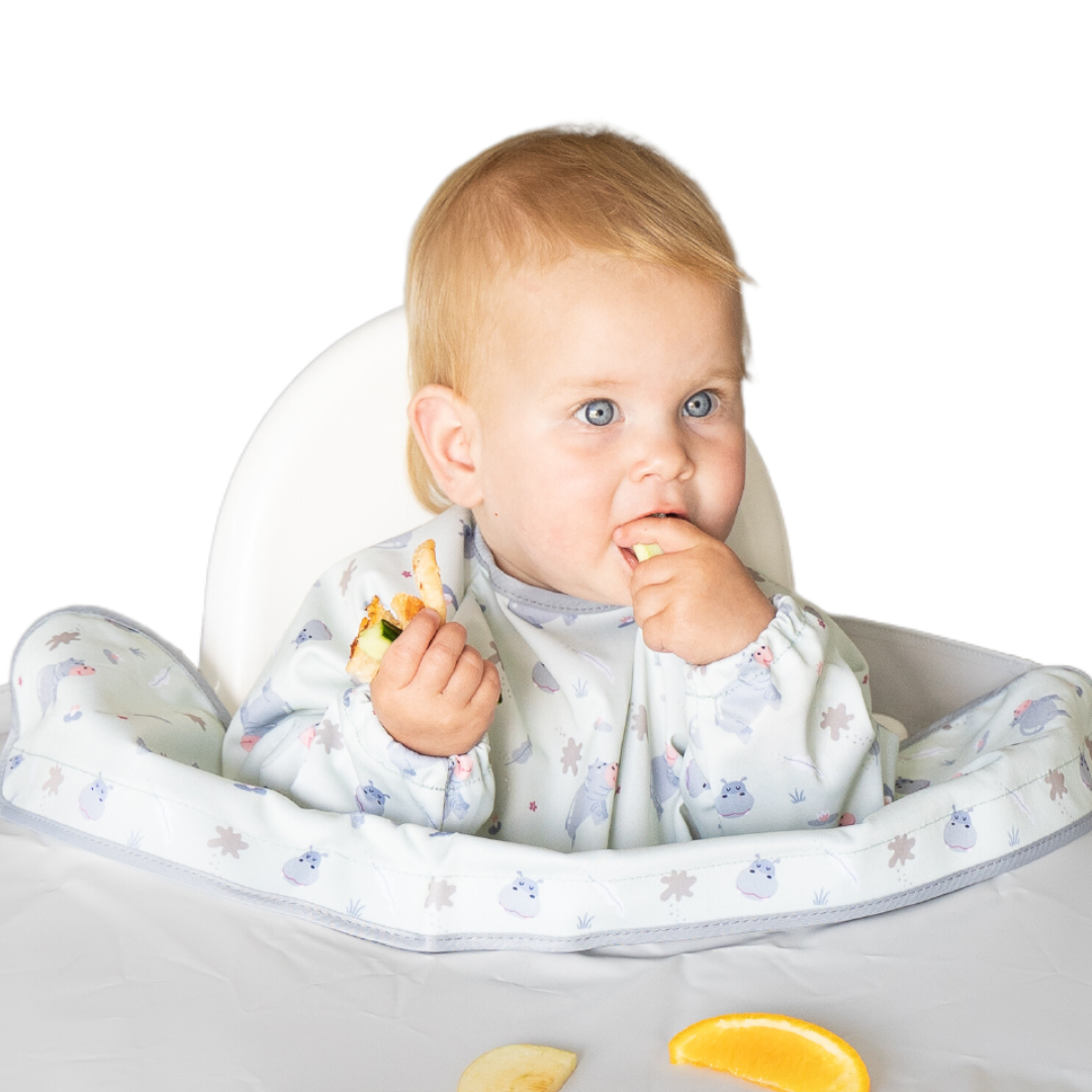 Baby eating on a highchair wearing overall long sleeve bib with hippo print