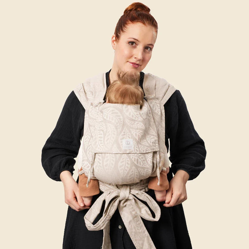 Mother carrying baby in Stokke Limas Carrier plus in valerian beige facing front.