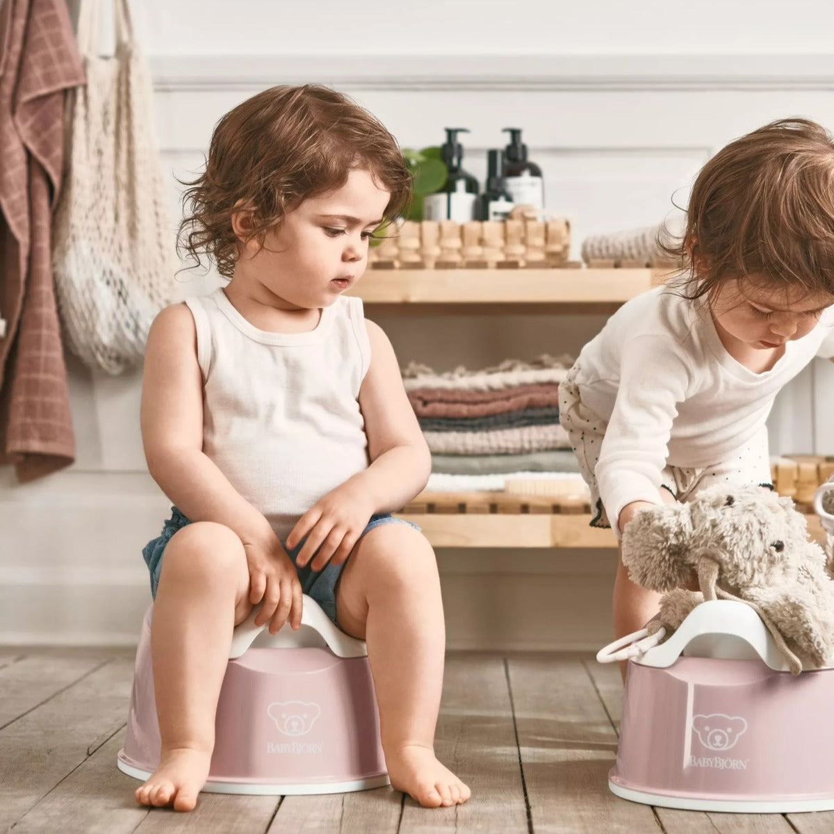 One boy sitting on Babybjorn Smart Potty in pink and another boy placing toy on it.