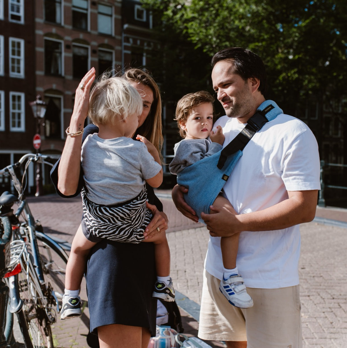 Mother and Father carrying babies with Wildride Toddler Carrier in Denim walking in a street