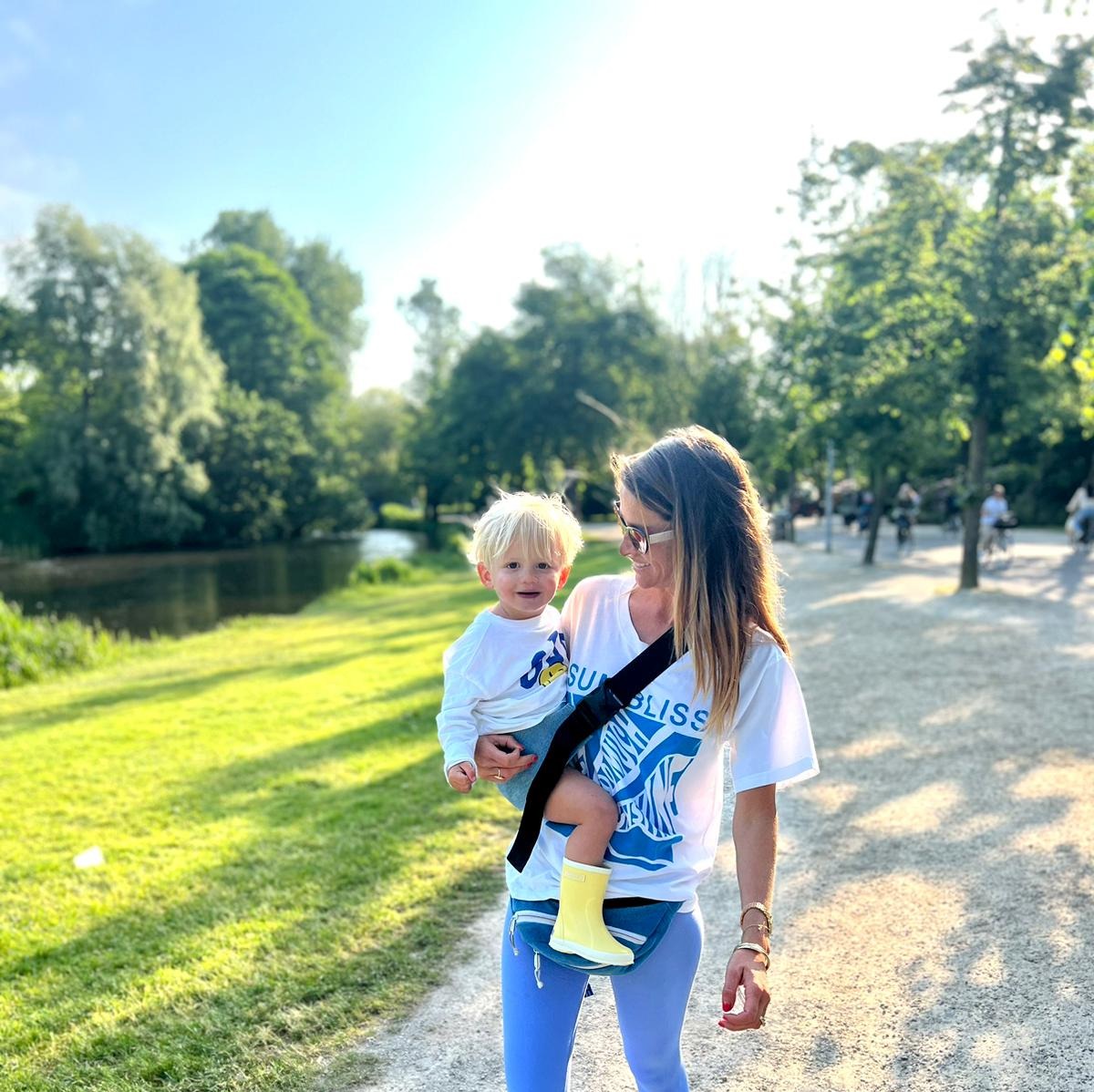 Mother carrying baby with Wildride Toddler Carrier in Denim walking in a park
