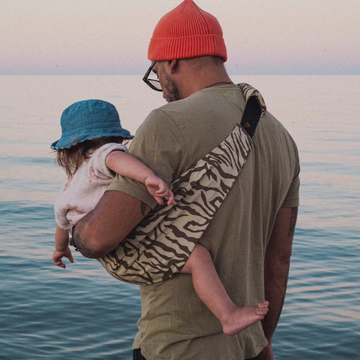 Father carrying toddler in Wildride Toddler Carrier in Zebra Print at beach