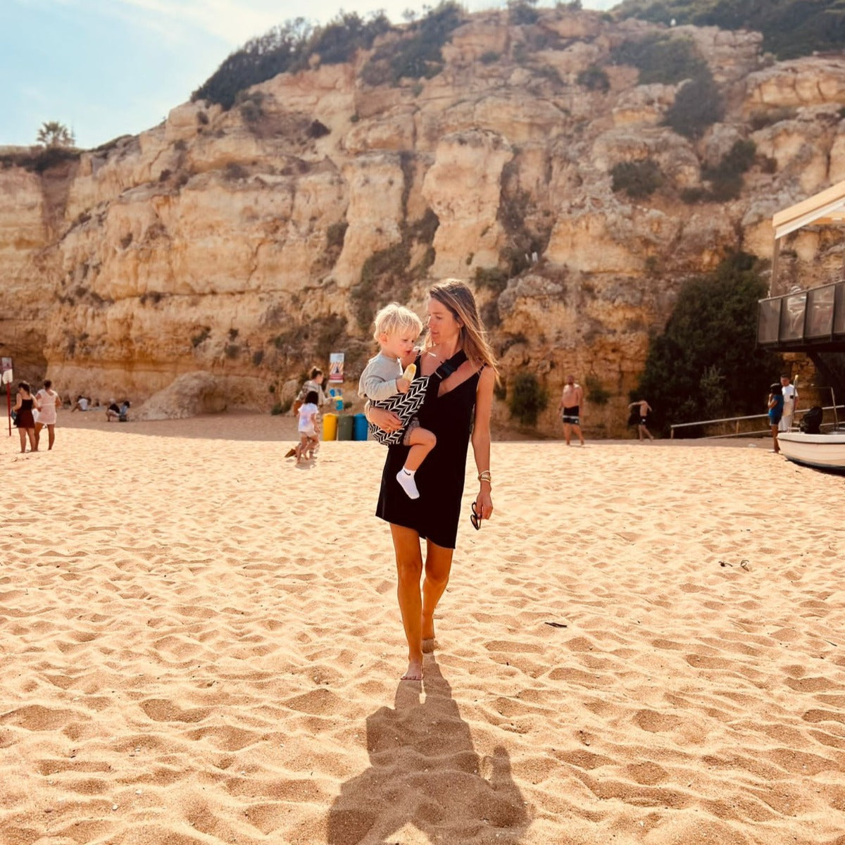 Mother walking on the beach while holding toddler with Wildride Toddler Carrier with Feather Print 