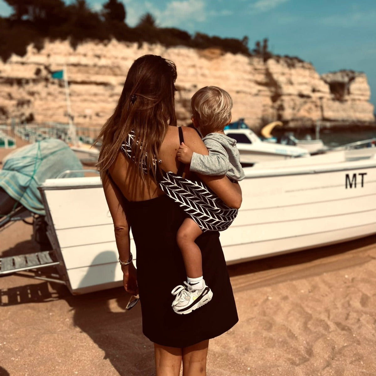 Mother holding toddler at the beach with Wildride Toddler Carrier with Feather Print back view