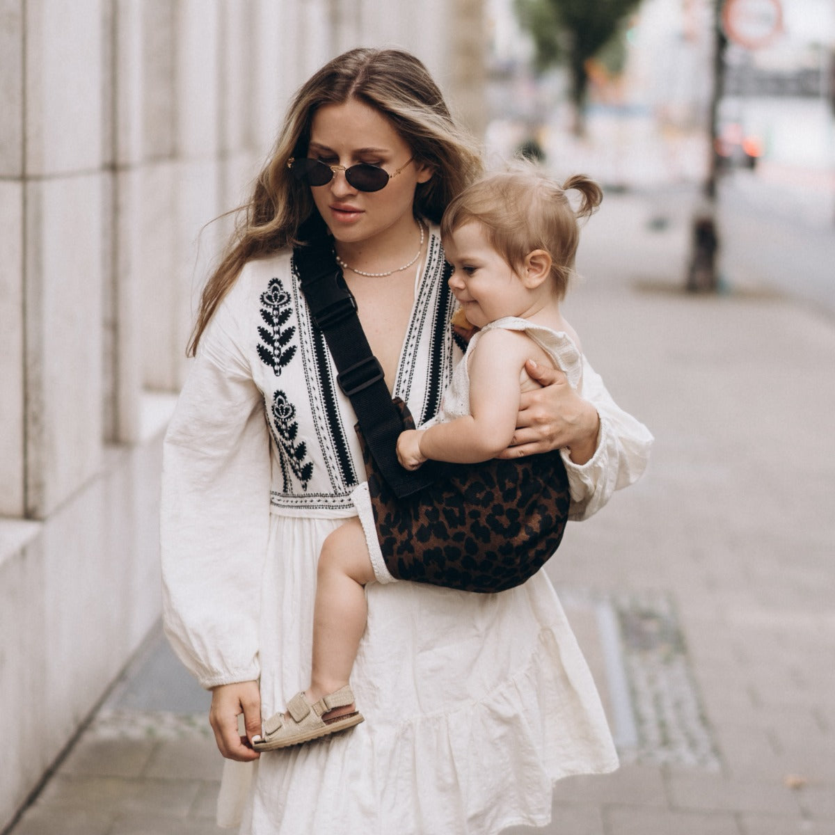Mother walking around the city wearing Wildride Toddler Carrier Brown Leopard to hold baby