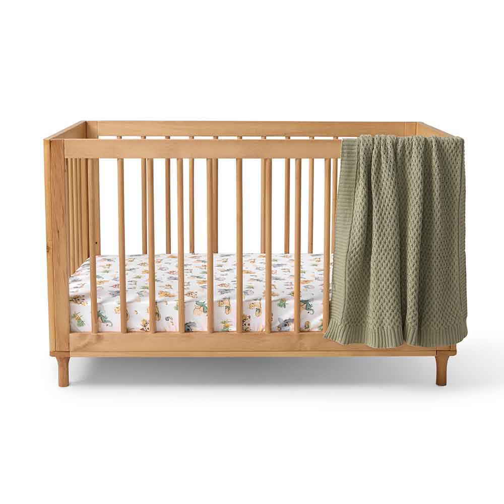 Snuggle Hunny organic cotton cot sheet in dragon print in cot with a hanging blanket
