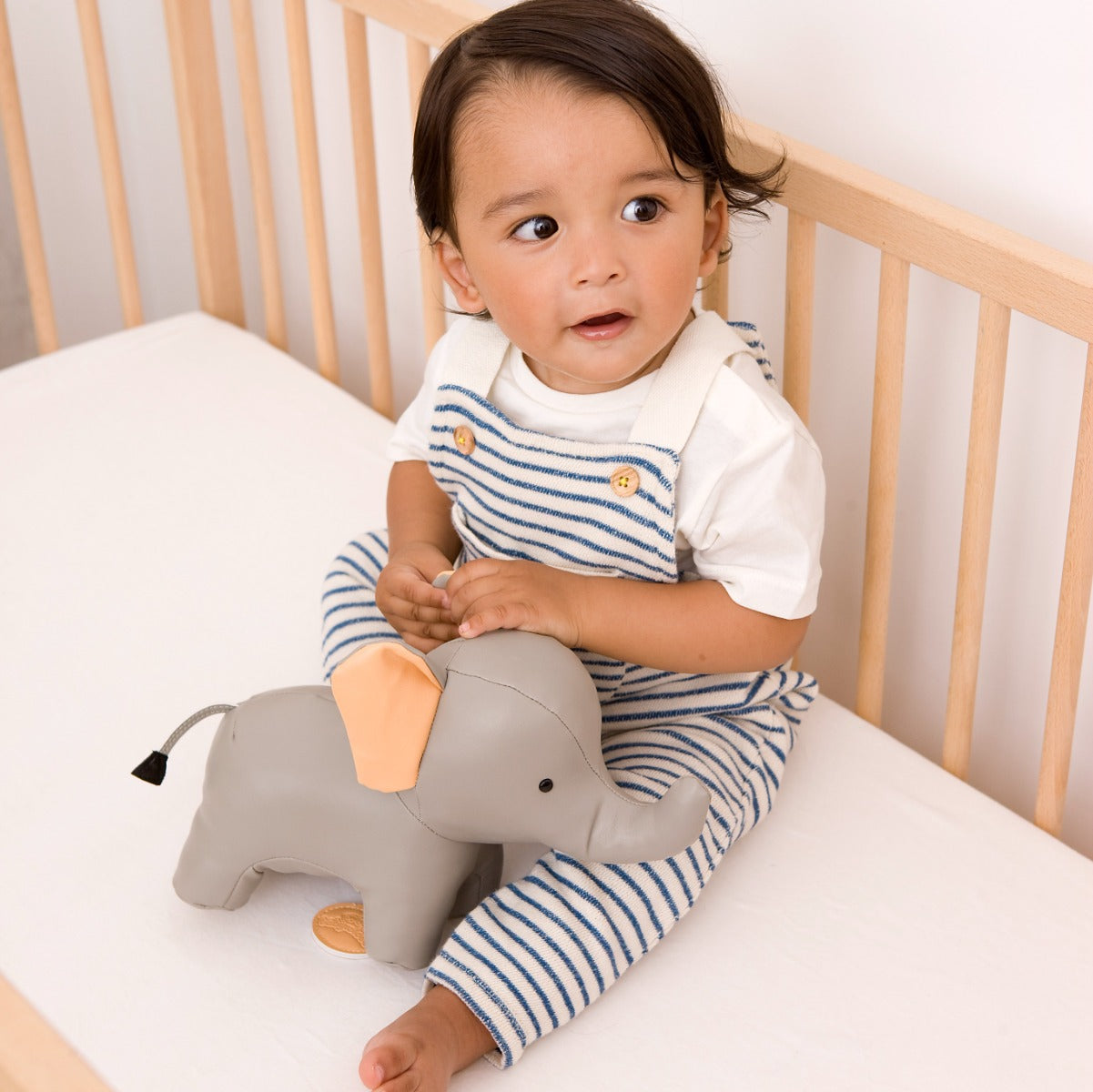 Baby in a cot holding Musical elephant toy in grey from little big friends