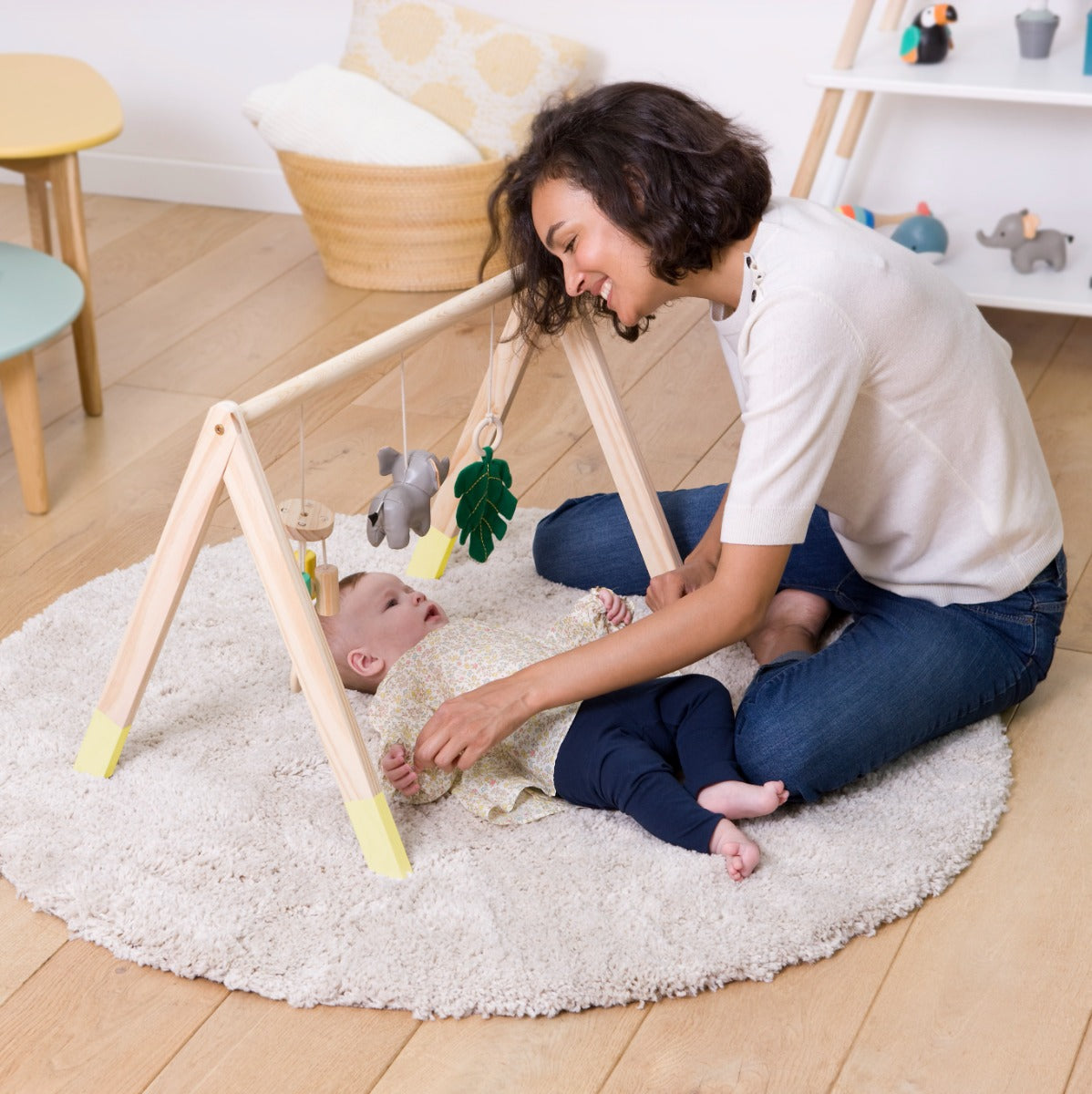 Baby girl lying and playing with Wooden Activity Gym with jungle theme, elephant, leaf and chime hanging and mother sitting beside her