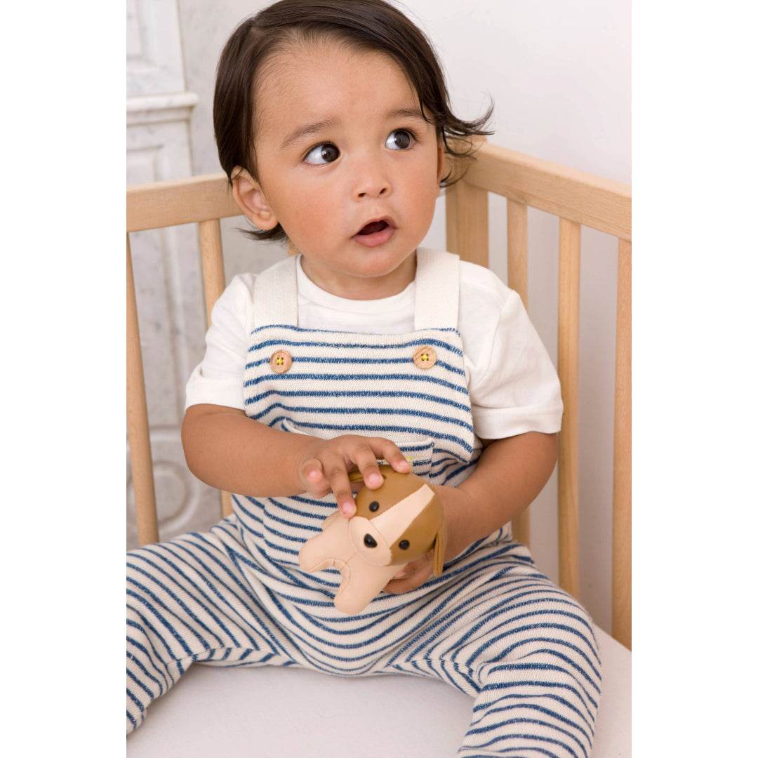 Baby boy holding Little Big Friends Tiny Friends Adrien the Dog sitting in a cot