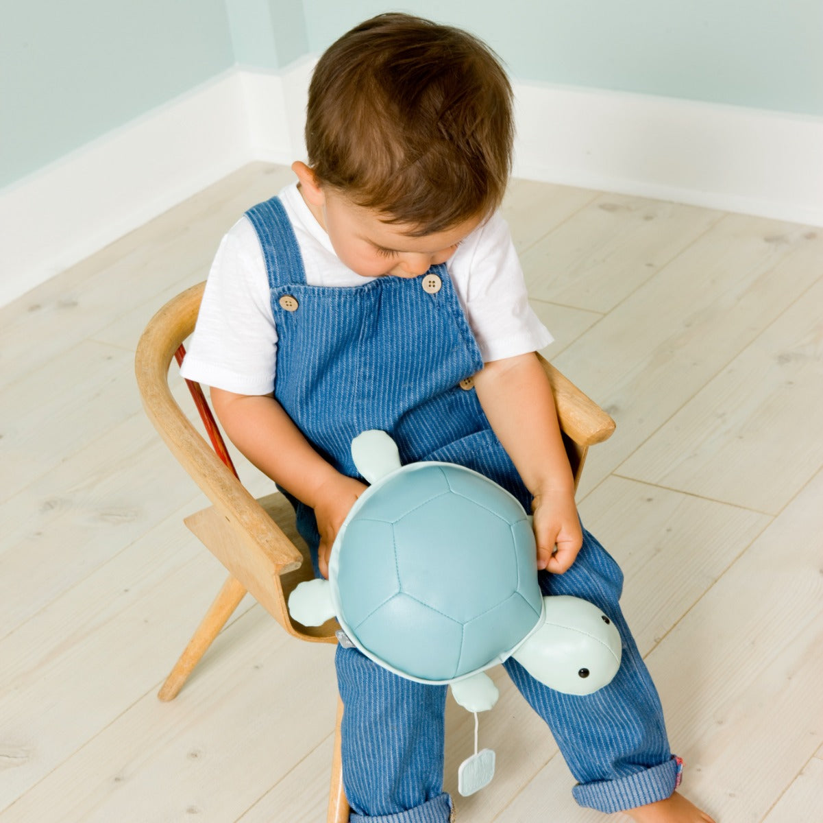 Baby holding Musical Friends - Emilie the Turtle from Little Big Friends siting on a chair 
