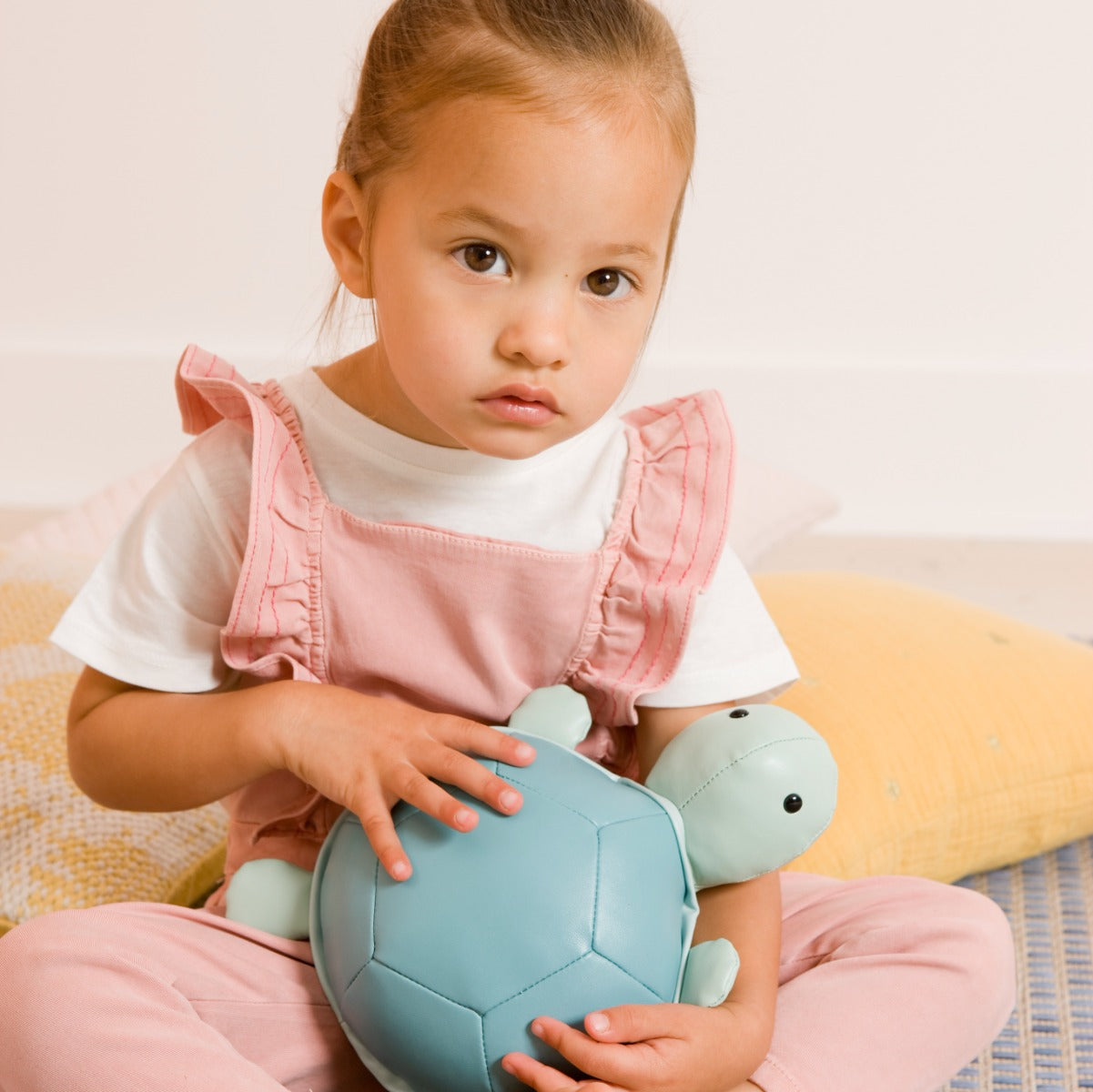 Baby girl holding Musical Friends - Emilie the Turtle from Little Big Friends sitting on a couch