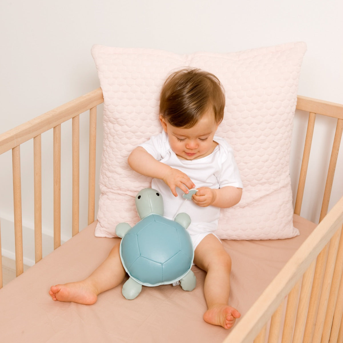 Baby holding Musical Friends - Emilie the Turtle from Little Big Friends sitting in a cot