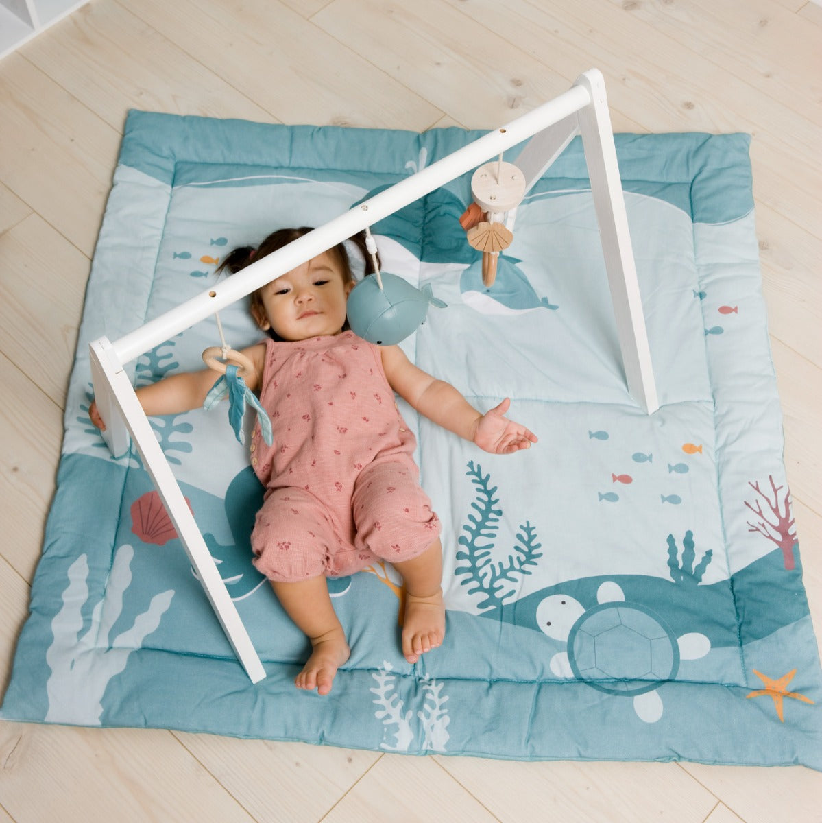 Little girl laying down and playing with Little big friends activity arch ocean and ocean mat