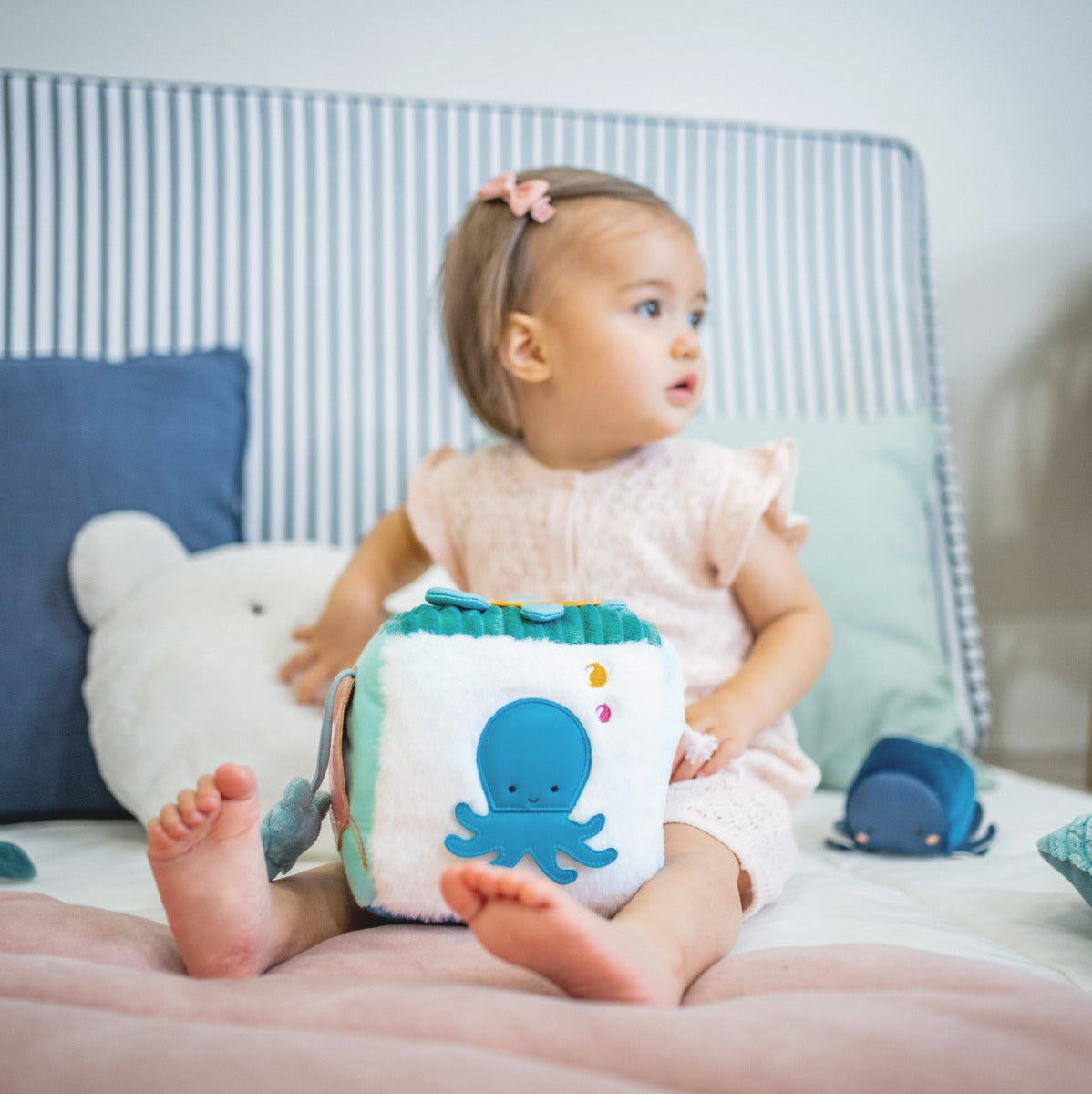 Baby girl sitting in bed with Little Big Friends Soft Activity Cube Ocean 